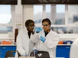 Two students in white lab coats holding a funnel and test tube
