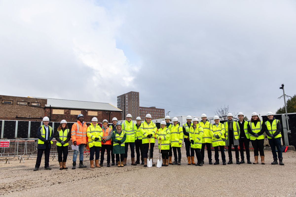 Group of people in high-visibility jackets and hard hats standing on a construction site with shovels.